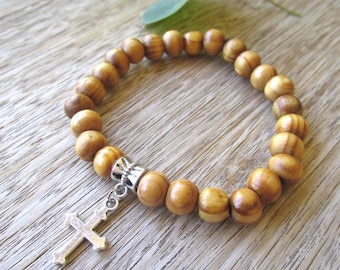 May include: A wooden bead bracelet with a silver cross charm. The beads are a light brown color with a wood grain pattern.