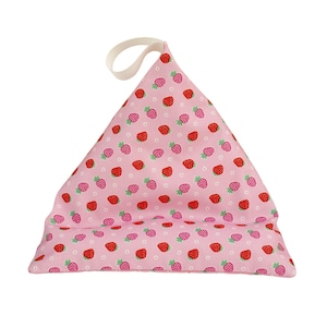 May include: A pink fabric book holder with a strawberry pattern. The holder is triangular in shape with a white loop at the top. The strawberries are red and pink with green leaves.