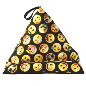 May include: Black triangular pillow with a yellow and black emoji pattern. The pillow is made of fabric and has a handle.
