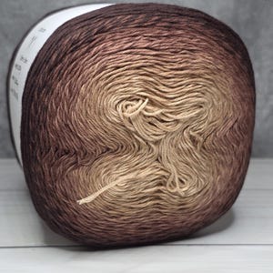 May include: A ball of yarn in a gradient of brown and beige tones. The yarn is tightly wound, with a visible strand extending from the centre. The yarn is likely used for knitting or crochet projects.