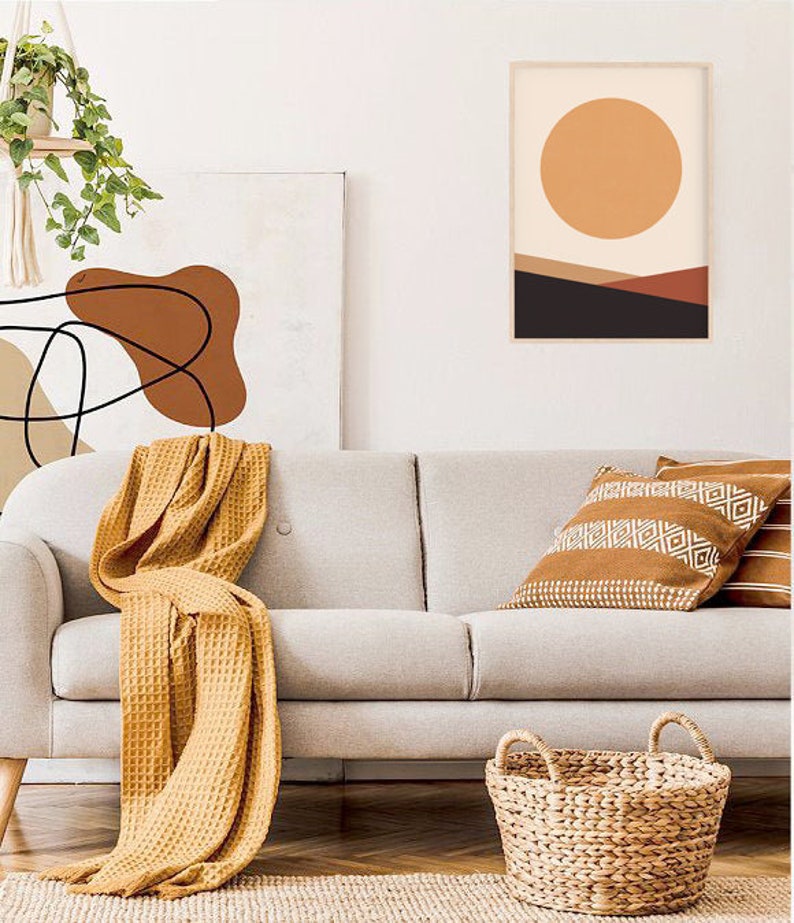 May include: A living room scene featuring a light gray sofa with a mustard yellow waffle-weave throw blanket. Decorative pillows with geometric patterns and a woven basket add texture. Artwork with abstract designs and a framed landscape print complete the decor.
