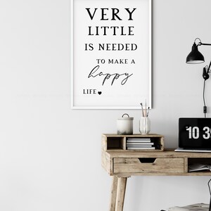 May include: A framed print with the text "VERY LITTLE IS NEEDED TO MAKE A happy LIFE" in black font. The print hangs above a wooden desk with a laptop, lamp, and decorative items.