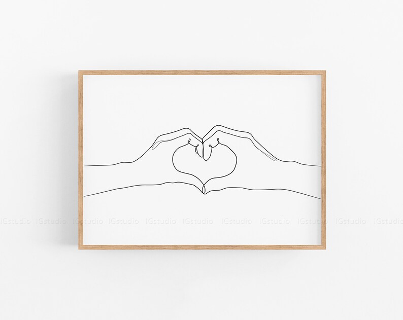 May include: A framed minimalist art print featuring a continuous line drawing of two hands forming a heart shape. The artwork is rendered in black against a white background, encased in a light brown wooden frame. The overall aesthetic is simple and elegant.