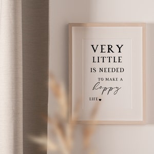May include: A framed print with the text "VERY LITTLE IS NEEDED TO MAKE A happy LIFE" in black font. The frame is light wood, and the background is a neutral color. The print is hanging on a white wall.