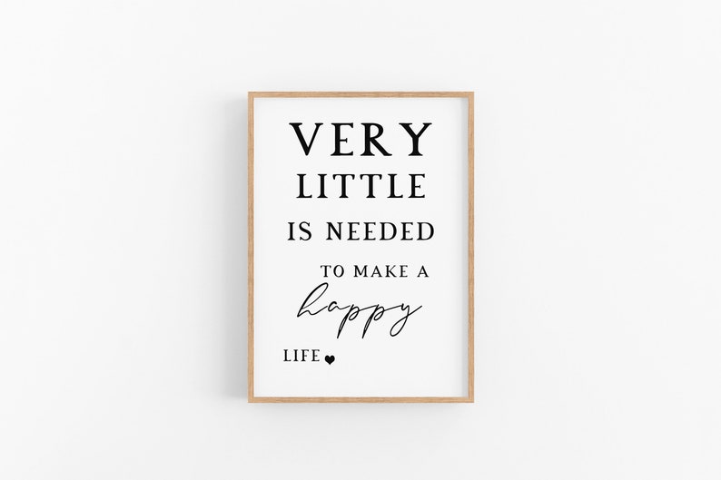 May include: A framed print with the text "VERY LITTLE IS NEEDED TO MAKE A happy LIFE." The text is in black against a white background, with a small heart symbol at the bottom. The frame is a light brown color.