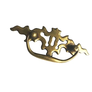 May include: A vintage brass drawer pull with an ornate, openwork design. The pull features a curved handle and decorative, leaf-like cutouts. The brass has a warm, aged patina, suggesting it is an antique or vintage piece.