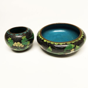 May include: Two small, round, black cloisonné bowls with green and white floral designs. The larger bowl has a turquoise blue interior.