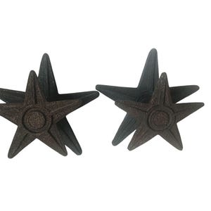 May include: Four dark brown star-shaped decorative objects. Each star has five points and a circular design in the center. The stars are made of a textured material and are arranged in pairs.
