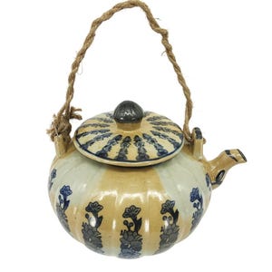 May include: A ceramic teapot with a beige and white body, adorned with blue floral patterns. It features a matching lid and a rope handle. The teapot is designed with a spout for pouring.