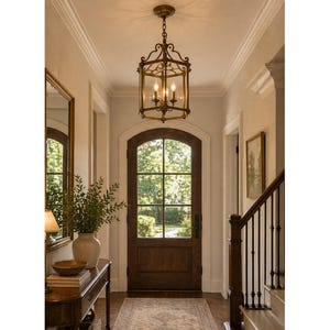 May include: An entryway featuring a decorative brass chandelier with four lights. A dark wooden door with glass panes is centered in the image. A table with a vase and mirror are on the left. The walls are painted a light color.