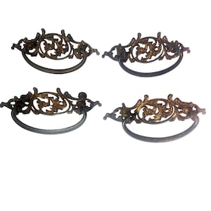 May include: Four antique drawer pulls with ornate, gold-toned floral designs and dark gray handles. The pulls are arranged in a square formation against a white background, showcasing their vintage aesthetic and decorative appeal.