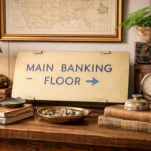 May include: A vintage-themed display featuring a sign that reads "MAIN BANKING FLOOR" with a blue arrow. The scene includes antique books, a brass lamp, a clock, and a map in a gold frame, creating a classic aesthetic.