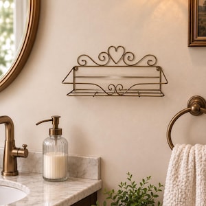 May include: A wall-mounted bronze-toned metal shelf featuring a decorative wire frame with a central heart shape and scrollwork accents. The rectangular storage rack has an open design with a flat base and a front rail, mounted on a wall.