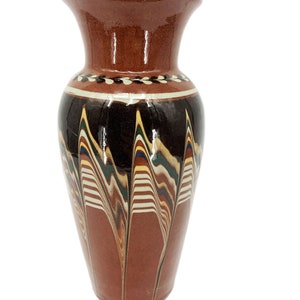 May include: A brown ceramic vase with a flared top and a decorative pattern. The vase features a dark brown base, a black central band with colorful wavy lines, and a white and brown band near the top.
