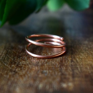 May include: A double-wrapped copper ring with a smooth, polished finish. The ring is made of a single piece of wire that is twisted and formed into a circle.