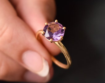 May include: A gold ring with a purple gemstone set in a prong setting.