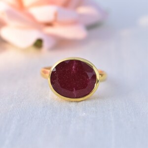 Pu&ograve; includere: Un anello d'oro con una grande pietra preziosa di forma ovale, di colore rosso intenso.