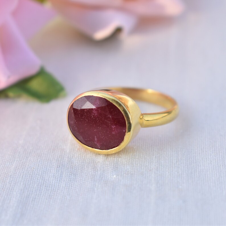 Pu&ograve; includere: Un anello d'oro con una grande pietra preziosa di rubino di forma ovale. Il rubino &egrave; di colore rosso intenso e ha una taglio sfaccettato.