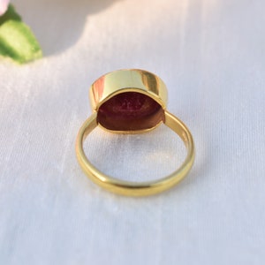 Pu&ograve; includere: Un anello d'oro con una grande pietra preziosa rossa incastonata al centro. L'anello &egrave; mostrato dal retro, quindi l'incastonatura &egrave; visibile.