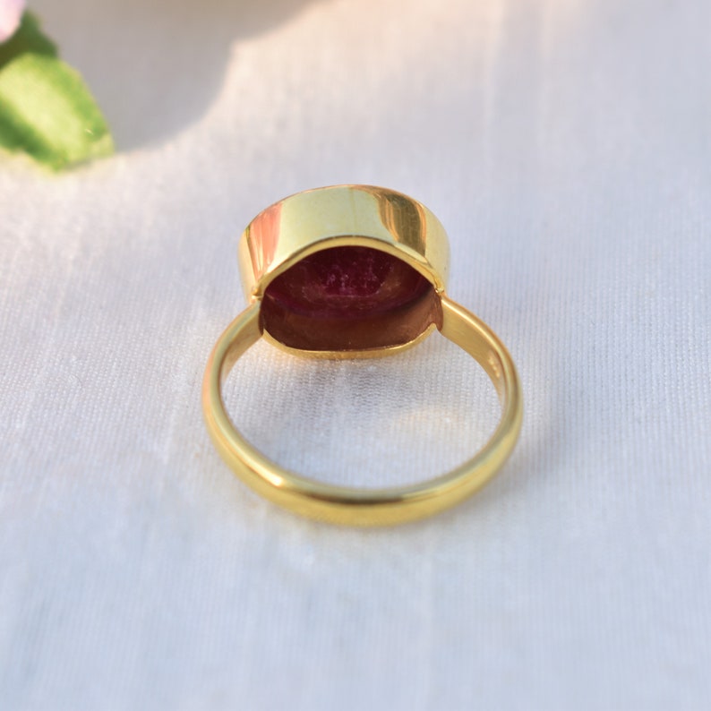 Pu&ograve; includere: Un anello d'oro con una grande pietra preziosa rossa incastonata al centro. L'anello &egrave; mostrato dal retro, quindi l'incastonatura &egrave; visibile.