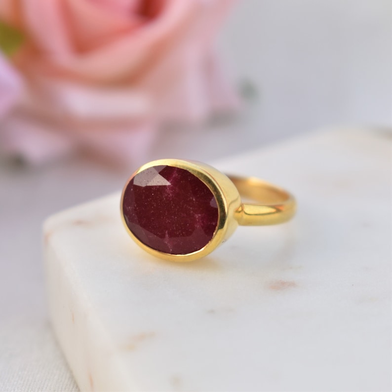 Pu&ograve; includere: Un anello d'oro con una grande pietra preziosa di rubino di forma ovale. Il rubino &egrave; di colore rosso intenso e ha una taglio sfaccettato.