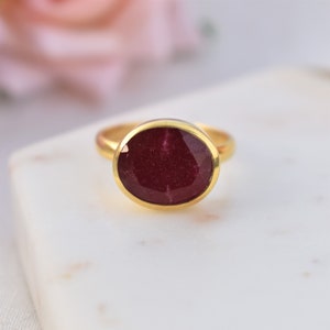 Pu&ograve; includere: Un anello d'oro con una grande pietra preziosa di forma ovale, di colore rosso intenso.