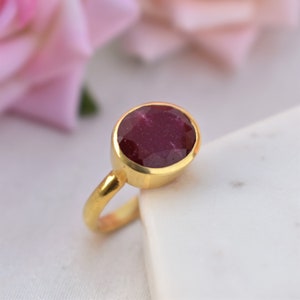 Pu&ograve; includere: Un anello d'oro con una grande pietra preziosa di rubino di forma ovale. Il rubino &egrave; di colore rosso intenso e ha una taglio sfaccettato.