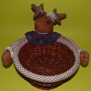 May include: A brown wicker basket with a reindeer face and plaid fabric lining. The basket has a checkered brown and white fabric trim.
