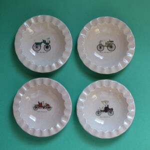 May include: Set of four small, white ceramic ashtrays with a scalloped edge. Each ashtray features a vintage car illustration.