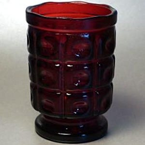 May include: A ruby red glass tumbler with a textured, geometric pattern. The vintage drinking glass has a cylindrical shape with a slightly flared rim and a small, circular base. The glass is approximately 4 inches tall.