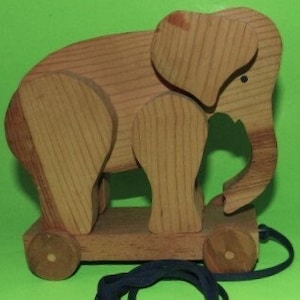 May include: A wooden toy elephant with wheels and a pull string. The elephant is brown and has a simple design.