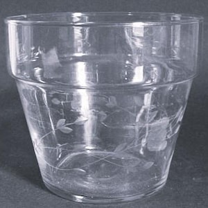 May include: A clear glass tumbler with a slightly flared shape and a decorative etched floral design. The glass has a thick base and a band around the middle. The glass is empty and sits on a dark surface.