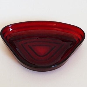 May include: A red glass dish with a scalloped edge and a concentric circle design. The dish is perfect for serving snacks or holding jewelry.