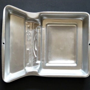 May include: A silver metal cake pan shaped like a book. The pan has a detailed design on the front cover.