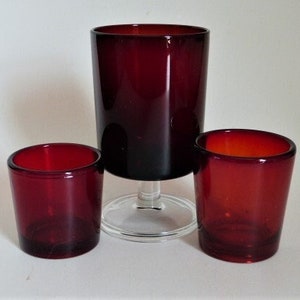May include: Three red glass cups, one tall and two short, on a white background.