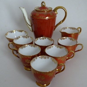 May include: A red and gold tea set with a teapot, creamer, and six cups. The set has a floral design with gold accents.
