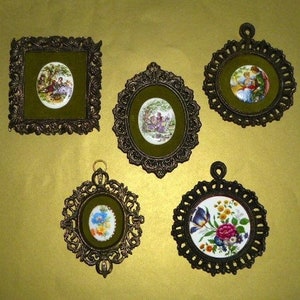 May include: Five ornate gold-toned frames with intricate designs, each holding a small porcelain picture. The pictures feature floral patterns and scenes of people in period clothing.