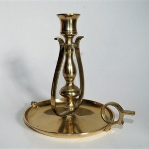 May include: A gold metal candle holder with a decorative design. The holder has a round base and a tall, slender stem with a cup at the top for holding a candle.