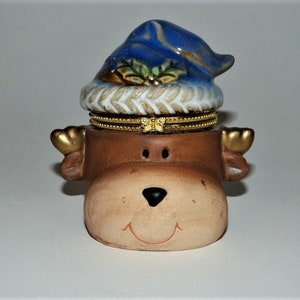 May include: A ceramic trinket box shaped like a reindeer's head with a blue and white Santa hat. The reindeer has a brown face with gold antlers.
