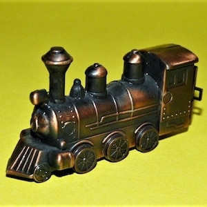 May include: A vintage-style metal toy train with a brown and black finish. The train has a large smokestack, a bell, and a detailed engine. The train is a pencil sharpener.