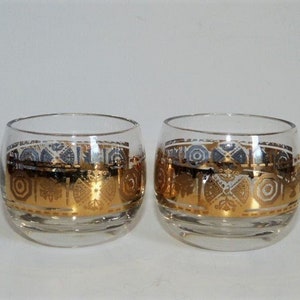 May include: Two clear glass tumblers with gold and white geometric designs. The glasses are round and have a wide base.