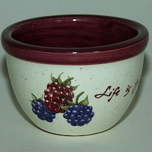 May include: A white ceramic bowl with a burgundy rim and a speckled glaze. The bowl has a painted design of blackberries and raspberries with the text "Life is Sweet" in burgundy.