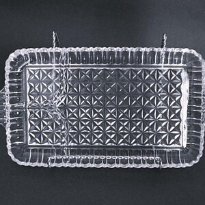 May include: A clear glass serving tray with a decorative, geometric pattern. The tray has a raised edge and two handles on the sides.