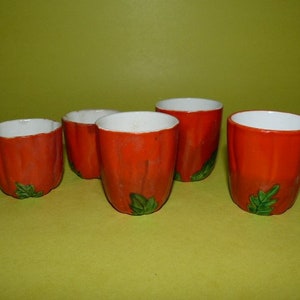 May include: Set of four orange ceramic cups with green leaf designs. The cups are all the same size and shape, and they have a white interior.