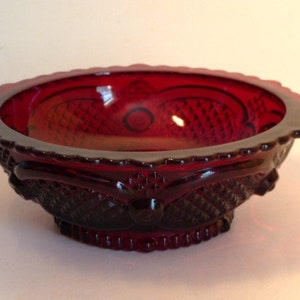 May include: A red glass bowl with a diamond pattern and a scalloped edge. The bowl is made of ruby red glass and has a vintage look.