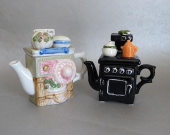 May include: Two ceramic teapots shaped like kitchen appliances. The first teapot is shaped like a vintage stove with a white and green design. The second teapot is shaped like a black stove with a white oven door and a green top.