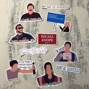 May include: A set of ten stickers featuring characters and quotes from the television show Parks and Recreation. The stickers are printed on white vinyl with black outlines and feature a variety of colours, including red, blue, and green.