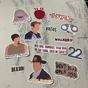 Puede incluir: Un conjunto de 10 pegatinas con personajes y frases de la serie de televisión The Walking Dead. Las pegatinas están impresas en vinilo blanco con texto rojo, negro y gris. Las pegatinas incluyen frases como "Little Girl?", "Pizza Delivery Boy", "Vatos", "Walkers!" y "Don't Dead Open Inside".