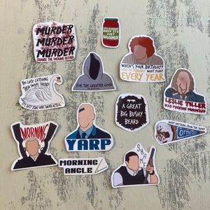 May include: A collection of 11 stickers featuring various designs and text. The stickers are on a light brown wooden surface. Some of the stickers include text such as "Murder Murder Murder", "For the Greater Good", "A Great Big Bushy Beard", "When's your birthday? 22nd of February what year? Every year", "Leslie Tiller was fucking murdered", "Morning Angle", "Yarp", "Morning", "It's alright Andy it's just Bolognese", "No luck catching them swans then? It's just the one swan actually", and "Want anything from the shop? Ornetto".
