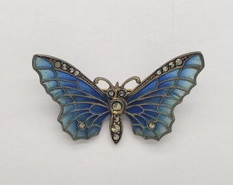 May include: A blue and silver butterfly brooch with marcasite stones. The butterfly's wings are detailed with a delicate pattern and the body is adorned with marcasite stones.